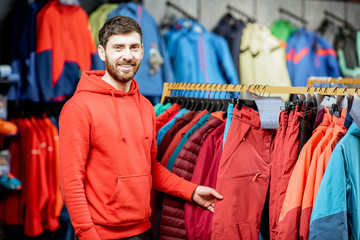 Portrait of a handsome man standing as a seller or customer in the clothing department with jackets in a sports shop © rh2010