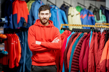 Portrait of a handsome man standing as a seller or customer in the clothing department with jackets...