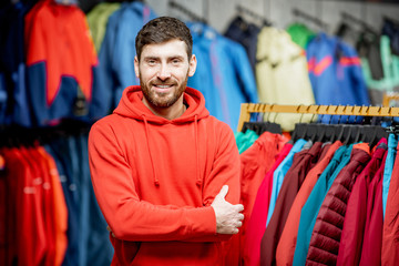 Portrait of a handsome man standing as a seller or customer in the clothing department with jackets in a sports shop