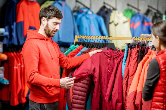 Man choosing winter clothes picking up down jackets on the hanger in the sports shop