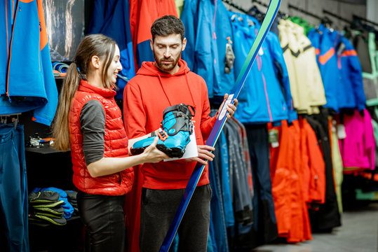 Man and woman choosing sports equipment looking on the ski and boots for skiing in the shop