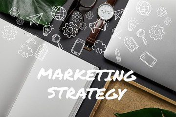Flat lay with open notebook and laptop on black background with "marketing strategy" lettering and icons