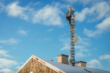 Fototapeta na wymiar Telecom worker repairing antenna tower on blue sky background, cellular tower system.