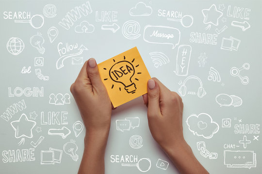 cropped image of woman holding paper sticker with word idea in lightbulb on white with marketing icons