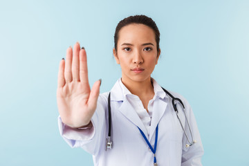 Doctor posing isolated over blue wall background with stethoscope showing stop gesture.