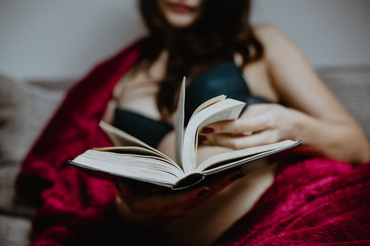 Woman in underwear with a red blanket holding a book