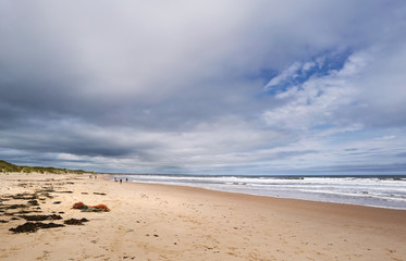 Fototapeta na wymiar DRURIDGE BAY, ENGLAND, UK - JUNE 03, 2016: People walking along the golden sands of Druridge Bay in Northumberland, England.