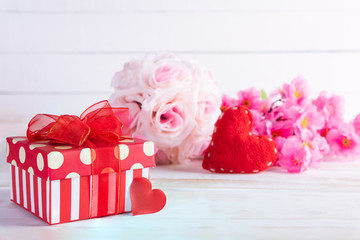 Valentines day and love concept. Pink gift box with handmade red heart and flowers on wooden block on white wooden background.