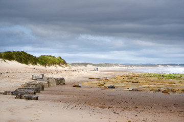 DRURIDGE BAY, ENGLAND, UK - JUNE 03, 2016: People walking along the golden sands of Druridge Bay in Northumberland, England.