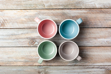 Fototapeta na wymiar Set of empty pastel colored mugs on grunge wood plank desk with copy space