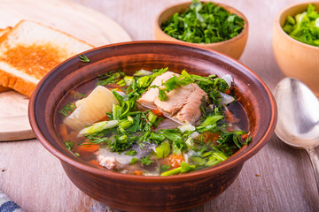 Salmon fillet fish soup with potatoes, tomatoes and carrots sprinkled with green onions and parsley in a glossy dish on a wooden table
