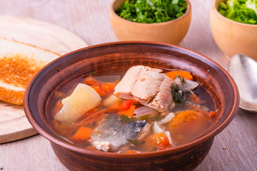Thick fish soup with potatoes, carrots, tomatoes and onions in a clay plate close-up