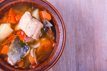 Thick fish soup with trout, potatoes, carrots, tomatoes and onions in a clay plate close-up, top...