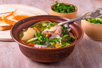 Salmon fillet fish soup with potatoes, tomatoes and carrots sprinkled with green onions and parsley in a glossy dish on a wooden table