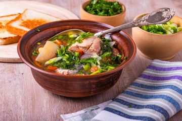 Salmon fillet fish soup with potatoes, tomatoes and carrots sprinkled with green onions and parsley in a glossy dish on a wooden table