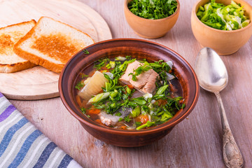 Salmon fillet fish soup with potatoes, tomatoes and carrots sprinkled with green onions and parsley in a glossy dish on a wooden table