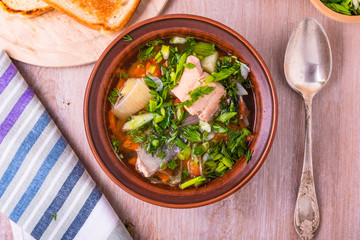 Salmon fillet fish soup with potatoes, tomatoes and carrots sprinkled with green onions and parsley in a glossy plate on a wooden table, top view