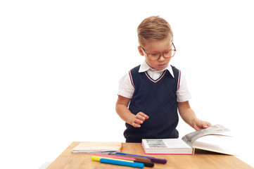 Little boy wearing glasses with trendy haircut standing with school stationery on white background