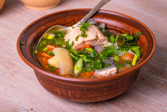 Salmon fillet fish soup with potatoes, tomatoes and carrots sprinkled with green onions and parsley in a glossy dish on a wooden table