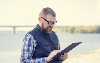 A man makes records about the state of water near the reservoir. Ecologist. Male middle age with a...
