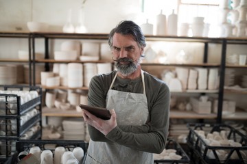 Serious potter using tablet surrounded by work