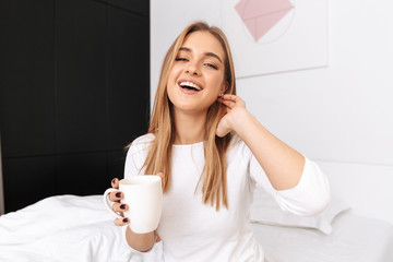 Happy young girl sitting on bed in the morning