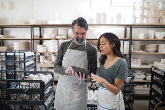 Smiling potter colleagues using tablet pc and talking