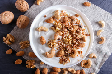 White plate with greek yogurt, granola, almond, cashew, walnuts  on black wooden background.
