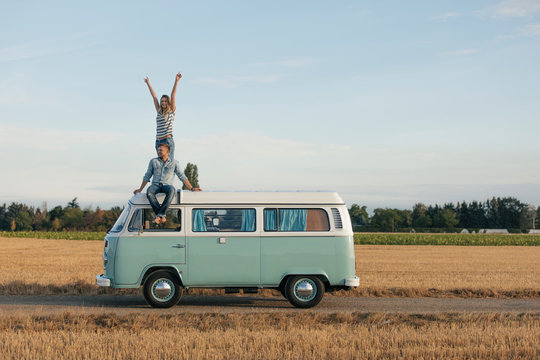 Happy couple on roof of a camper van in rural landscape