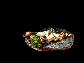 Some peaces of the cheese blue mold roquefort  with peaces of the nuts with parsley at the desk with black background