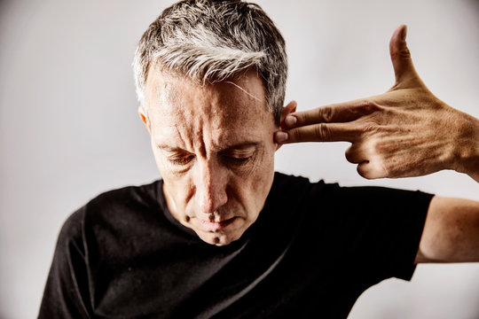 Portrait of mature man making shooting gesture with his hand against his temple