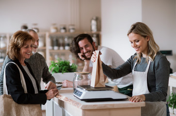 Senior couple buying groceries in zero waste shop, sales assistants serving them.