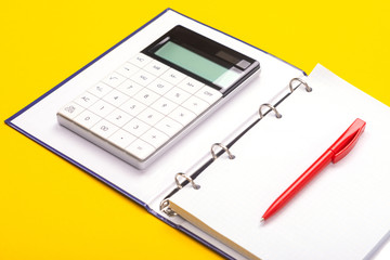Top view of working space table with calculator, notebook and pen isolated on yellow background