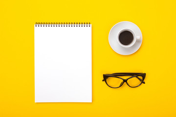 Working space with notebook, glasses and cup of coffee in morning isolated on yellow background