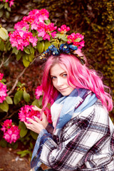 Fototapeta premium portrait of a beautiful girl with pink hair standing near pink flowers.