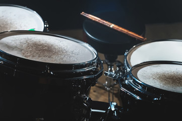 Fototapeta na wymiar Closeup view of a drum set and Drumsticks in a dark studio. Black drum barrels with chrome trim. The concept of live performances