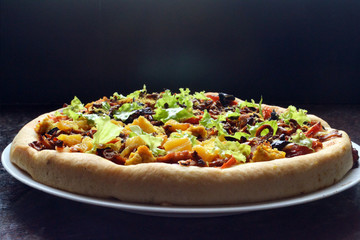 Thick, vegan pizza with tofu cheese, vegan soy sausages, mushrooms, capsicum, black olives, pineapple, tomatoes, lettuce and onions.