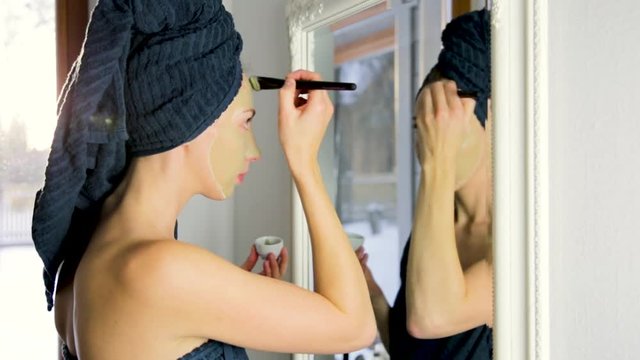 Beauty procedures skin care concept. Young woman applying facial gray and red mud clay mask to her face in bathroom. Woman with different masks on her face multi-masking