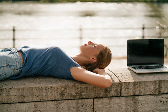 Young woman lying on a wall next to laptop