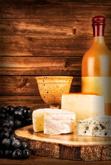 Bottle and glass of wine isolated on a wooden plank in background. Set of cheese on table.