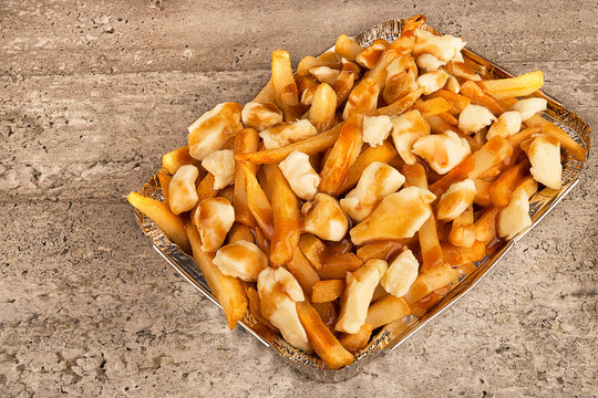 Close up on a poutine in a takeout container. Cooked with french fries, beef gravy and curd cheese.