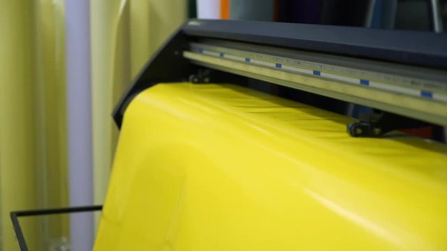 closeup long yellow vinyl rolling sheet moves through modern large format cutting appliance