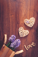 Two sisal hearts with love word and hyacinth flowers in a bag on rustic wooden background in flat lay with copy space. Birthday, Mother's, Valentines, Women's, Wedding Day concept.