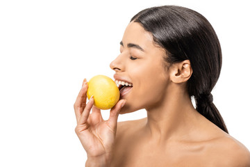 Obraz na płótnie Canvas smiling naked african american girl with closed eyes biting lemon isolated on white