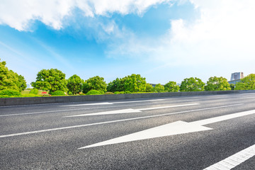 Urban asphalt road and green trees under blue sky