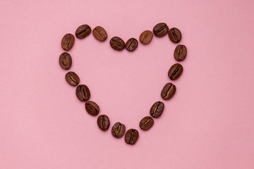 Coffee beans in heart shape on pink background. Copy spase