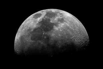 First quarter Moon isolated in the dark space, with its craters and shadows, taken with telescope.