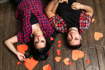 Top view of happy valentines couple is lying on the wooden floor with red paper hearts looking at...