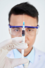 Young doctor holding syringe with red liquid