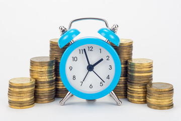 Clock in the foreground, stacks of coins in the background